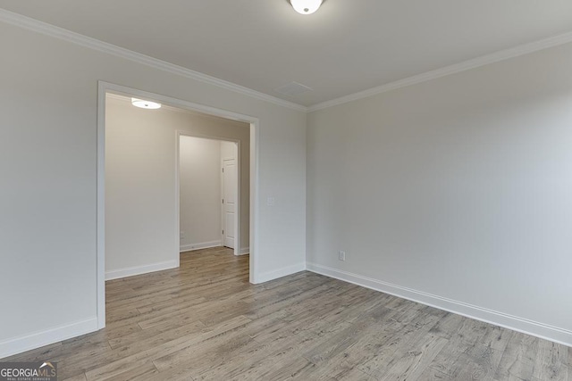 empty room with crown molding, light wood-style flooring, and baseboards