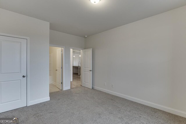 unfurnished bedroom featuring light colored carpet, baseboards, and ensuite bathroom