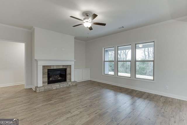 unfurnished living room with visible vents, light wood-style flooring, ornamental molding, a stone fireplace, and baseboards