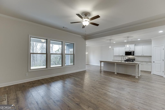 kitchen with decorative light fixtures, stainless steel appliances, light countertops, white cabinetry, and a kitchen island with sink