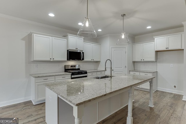 kitchen featuring hanging light fixtures, appliances with stainless steel finishes, a kitchen island with sink, white cabinets, and a sink