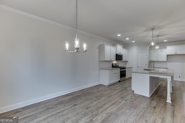 kitchen featuring pendant lighting, stainless steel appliances, white cabinetry, a sink, and an island with sink