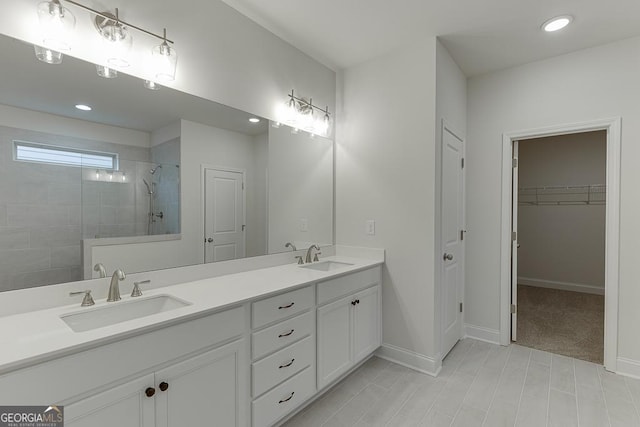 full bath with a walk in closet, a sink, a tile shower, and double vanity