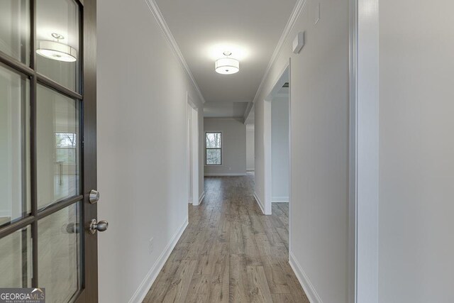 hallway featuring baseboards, light wood-type flooring, and crown molding