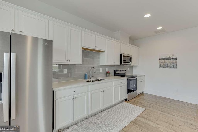 kitchen with stainless steel appliances, light countertops, backsplash, white cabinets, and a sink