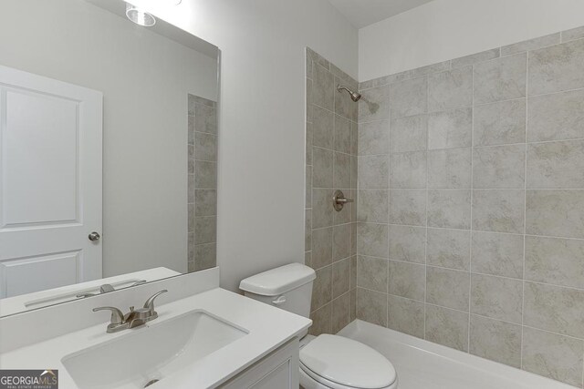 bathroom featuring a tile shower, vanity, and toilet