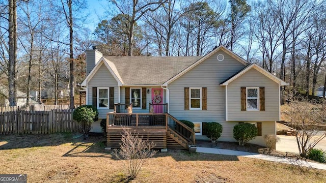 view of front of house featuring roof with shingles, fence, a chimney, and a front lawn