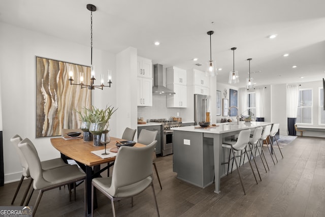 kitchen featuring decorative light fixtures, high end appliances, light countertops, a kitchen island with sink, and wall chimney range hood