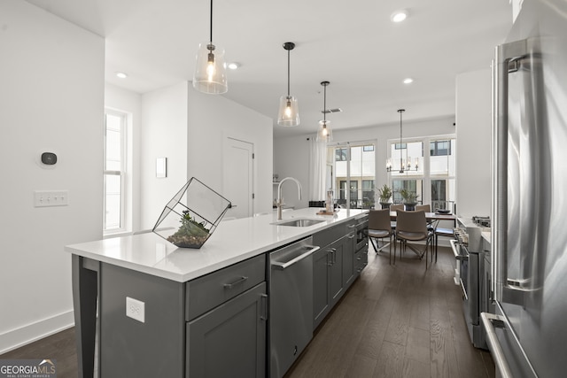 kitchen with light countertops, hanging light fixtures, appliances with stainless steel finishes, a sink, and an island with sink