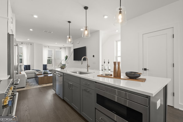 kitchen featuring a center island with sink, gray cabinetry, appliances with stainless steel finishes, open floor plan, and a sink