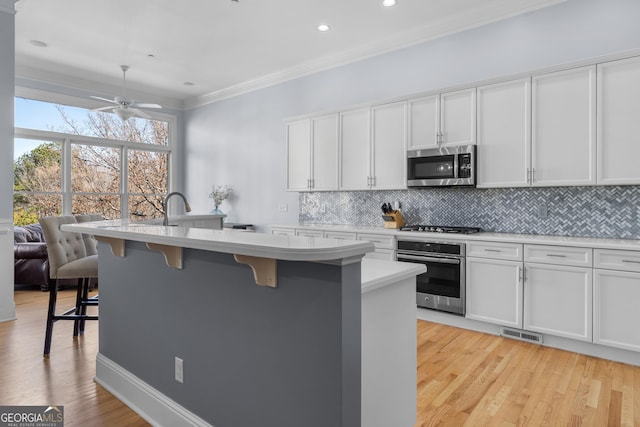 kitchen featuring a center island with sink, light countertops, appliances with stainless steel finishes, white cabinets, and a kitchen breakfast bar