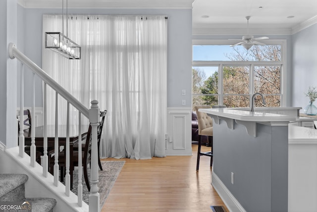 interior space featuring visible vents, wainscoting, ornamental molding, wood finished floors, and ceiling fan with notable chandelier