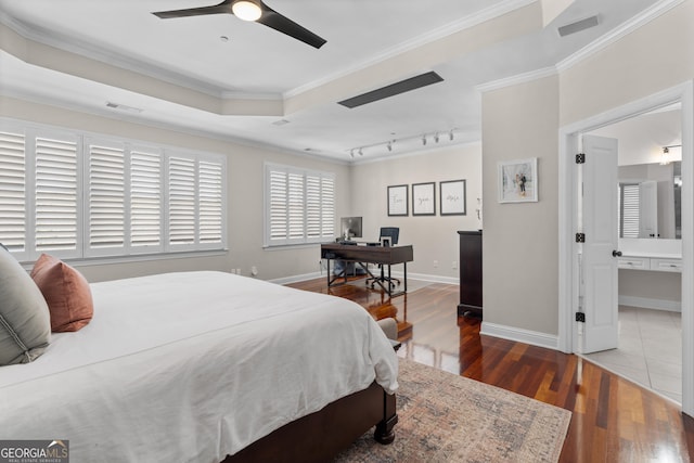 bedroom featuring wood finished floors, visible vents, baseboards, a raised ceiling, and crown molding