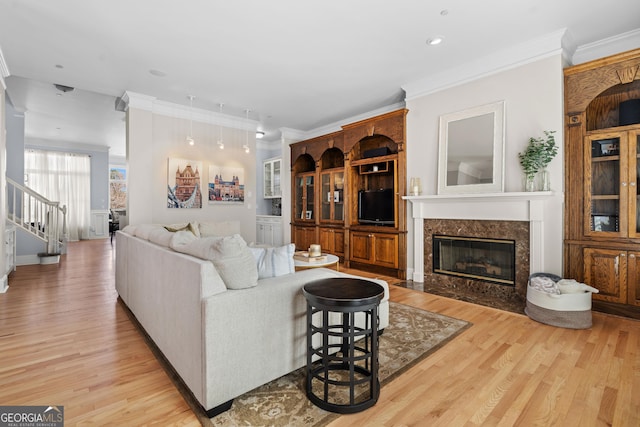 living room with light wood-type flooring, stairs, a fireplace, and ornamental molding