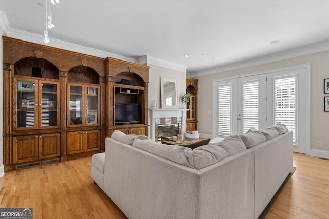 living area with visible vents, baseboards, light wood-style flooring, and crown molding