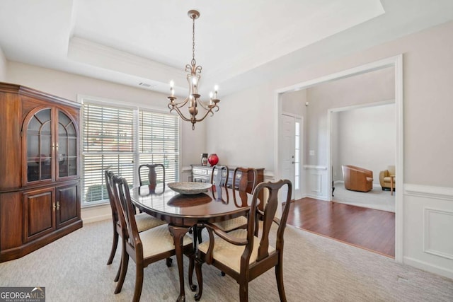 dining space featuring a chandelier, light carpet, visible vents, wainscoting, and a tray ceiling