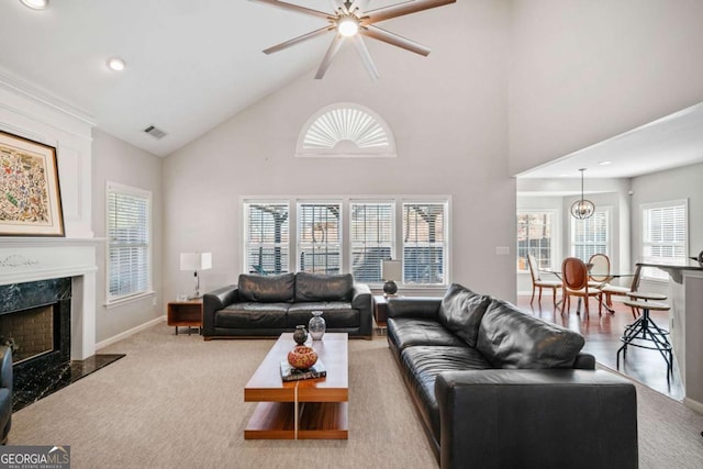 living area featuring baseboards, visible vents, light colored carpet, a premium fireplace, and high vaulted ceiling