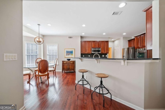 kitchen featuring dark wood-style floors, decorative light fixtures, visible vents, appliances with stainless steel finishes, and a kitchen bar