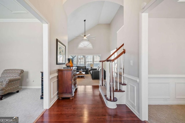 foyer with ceiling fan, wainscoting, dark carpet, and stairs