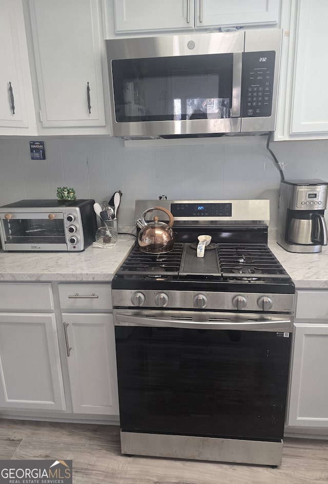 kitchen with backsplash, a toaster, light stone counters, white cabinets, and stainless steel appliances