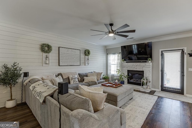 living room featuring dark wood-style floors, ornamental molding, a stone fireplace, and ceiling fan