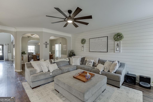 living area featuring ornamental molding, arched walkways, a ceiling fan, and wood finished floors