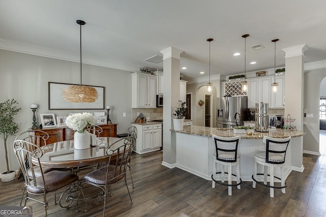 kitchen featuring arched walkways, decorative light fixtures, dark wood finished floors, stainless steel appliances, and white cabinetry