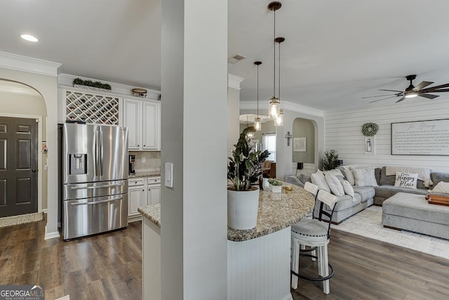 kitchen with light stone counters, white cabinets, open floor plan, stainless steel refrigerator with ice dispenser, and pendant lighting