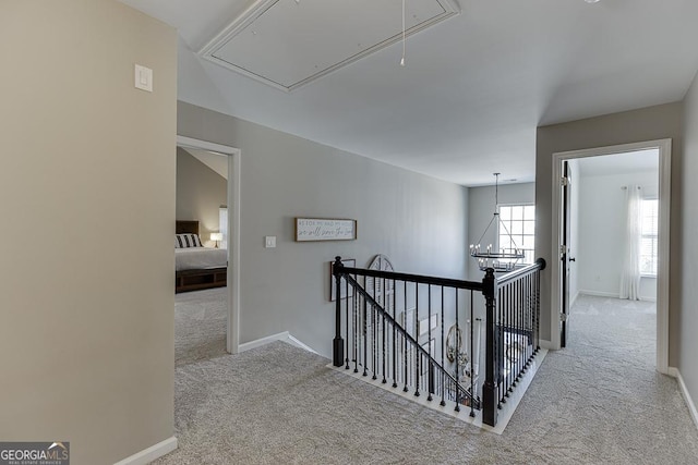 corridor with attic access, baseboards, light colored carpet, an upstairs landing, and a notable chandelier