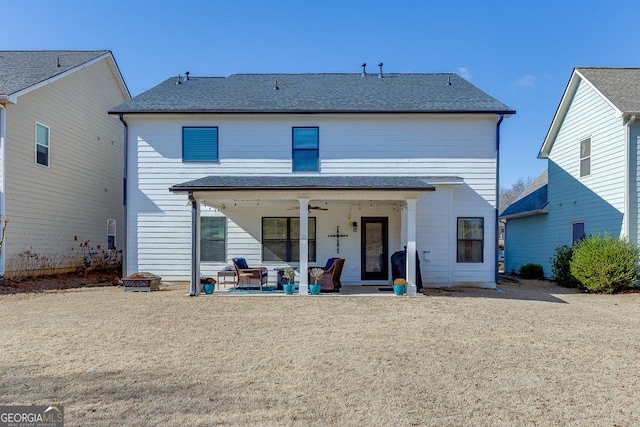 rear view of property with ceiling fan, a patio area, and a fire pit