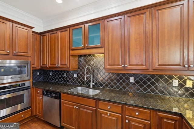 kitchen featuring stainless steel appliances, a sink, ornamental molding, tasteful backsplash, and dark stone countertops