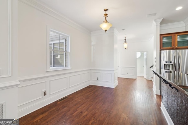 empty room with decorative columns, visible vents, dark wood-style floors, crown molding, and a decorative wall