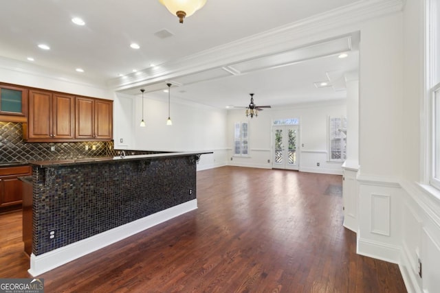 kitchen with a wainscoted wall, ornamental molding, brown cabinets, tasteful backsplash, and dark wood finished floors