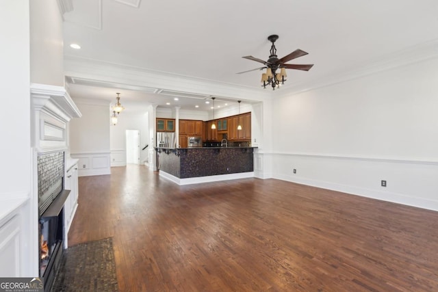 unfurnished living room featuring a decorative wall, dark wood-style flooring, a ceiling fan, a lit fireplace, and ornamental molding