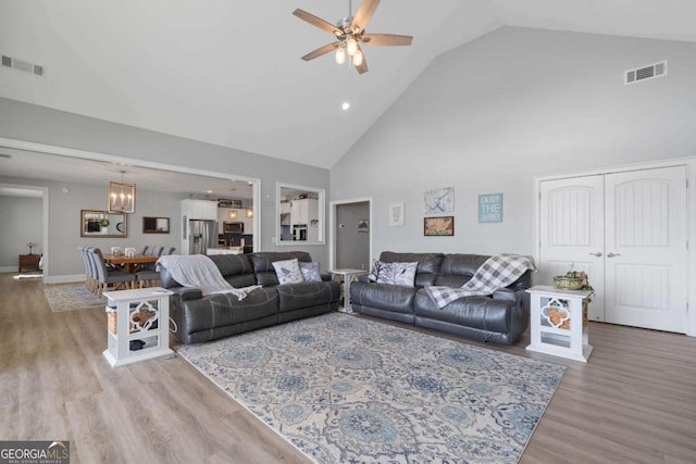 living room with light wood finished floors, visible vents, high vaulted ceiling, and ceiling fan with notable chandelier