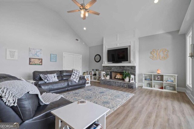 living room with ceiling fan, high vaulted ceiling, a fireplace, visible vents, and light wood-style floors