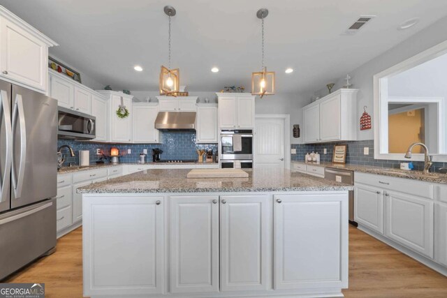 kitchen featuring stainless steel appliances, a kitchen island, white cabinets, and under cabinet range hood