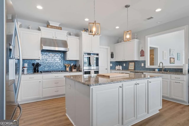 kitchen with under cabinet range hood, a kitchen island, white cabinetry, and stainless steel appliances