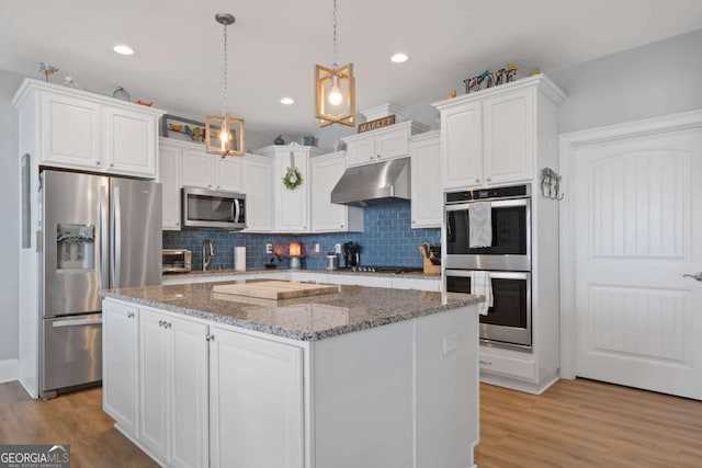 kitchen with under cabinet range hood, a kitchen island, white cabinetry, appliances with stainless steel finishes, and pendant lighting