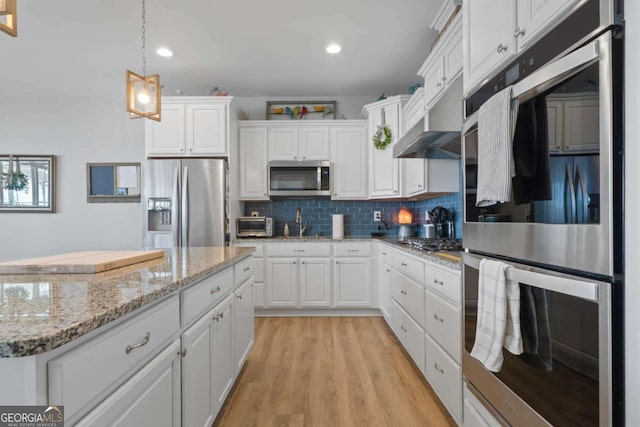 kitchen featuring stainless steel appliances, tasteful backsplash, hanging light fixtures, white cabinetry, and light wood-type flooring