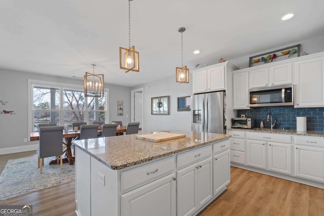 kitchen with decorative backsplash, decorative light fixtures, a center island, stainless steel appliances, and white cabinetry