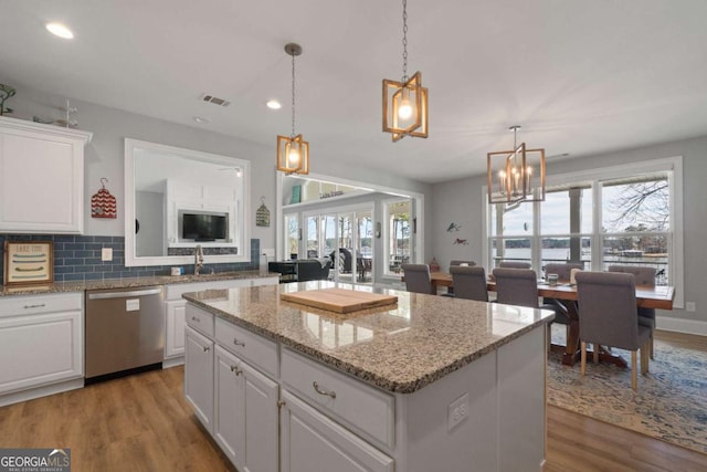 kitchen with hanging light fixtures, a kitchen island, white cabinets, and stainless steel dishwasher