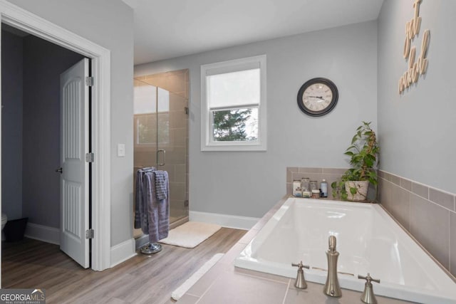 full bath with wood finished floors, a stall shower, a garden tub, and baseboards