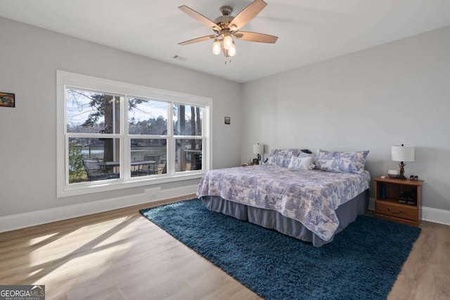 bedroom featuring a ceiling fan, visible vents, baseboards, and wood finished floors