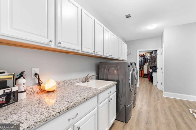 washroom with cabinet space, visible vents, light wood-style flooring, separate washer and dryer, and a sink