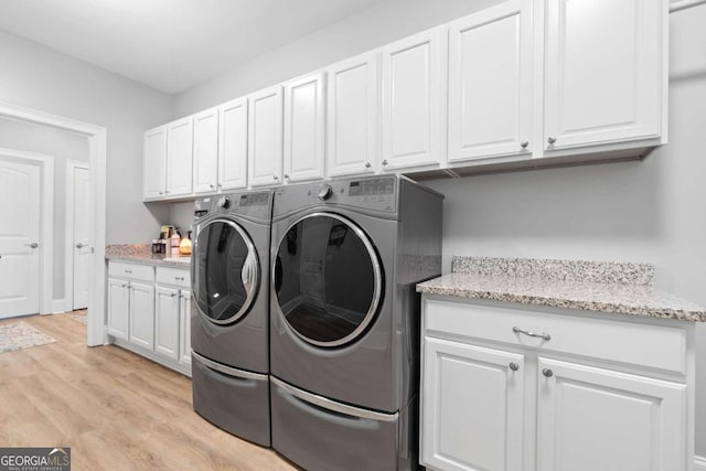 clothes washing area with light wood-style flooring, washer and clothes dryer, and cabinet space