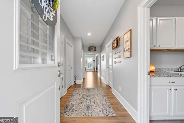 corridor with light wood-style floors, recessed lighting, a sink, and baseboards