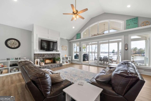 living room with ceiling fan, high vaulted ceiling, a stone fireplace, light wood-style flooring, and recessed lighting