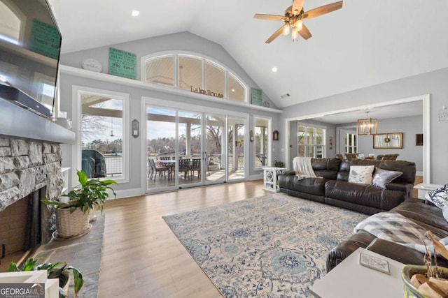 living room with ceiling fan with notable chandelier, light wood-type flooring, plenty of natural light, and a fireplace