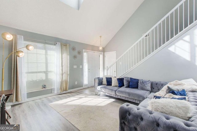 living area featuring high vaulted ceiling, stairway, light wood-style flooring, and baseboards